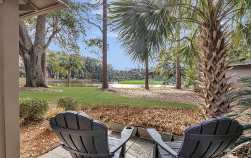 Adirondack chairs on a patio facing palms and a lagoon