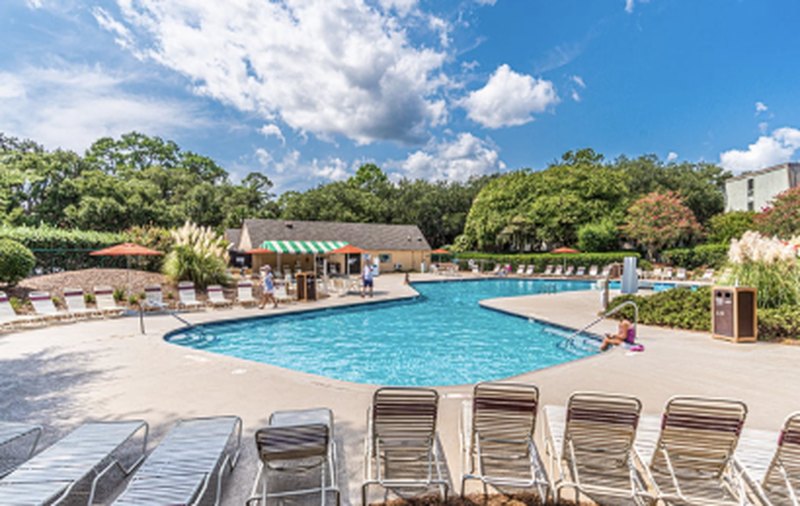 Resort pool lined with lounge chairs under a blue sky